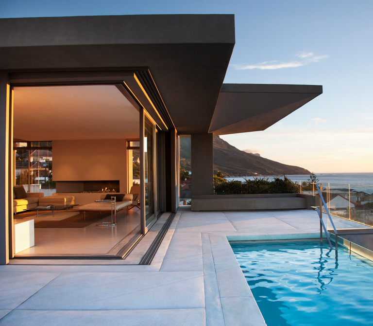 Casa moderna con piscina, ventanales de piso a techo y vista panorámica al mar al atardecer – FRANCO HomeServices