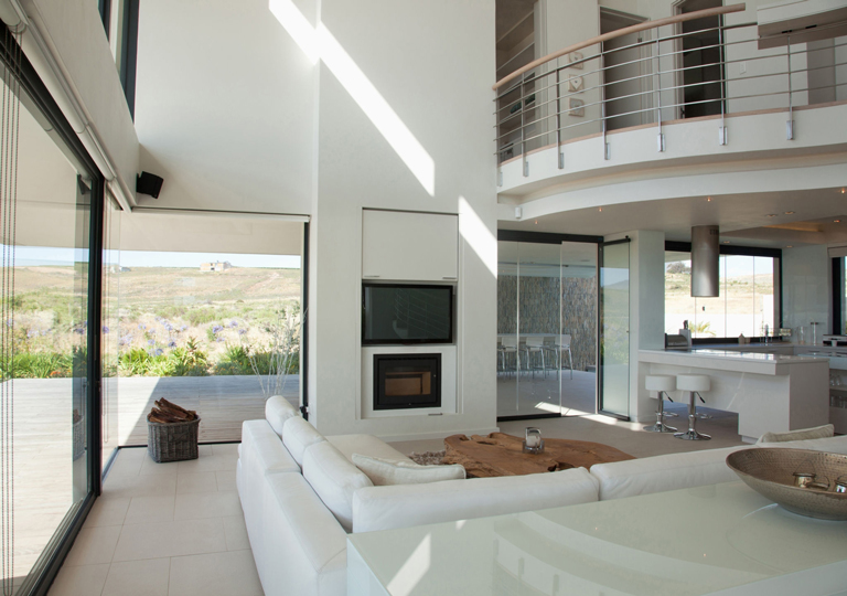 Sala de doble altura con chimenea moderna, cocina integrada, grandes ventanales y luz natural abundante – FRANCO HomeServices